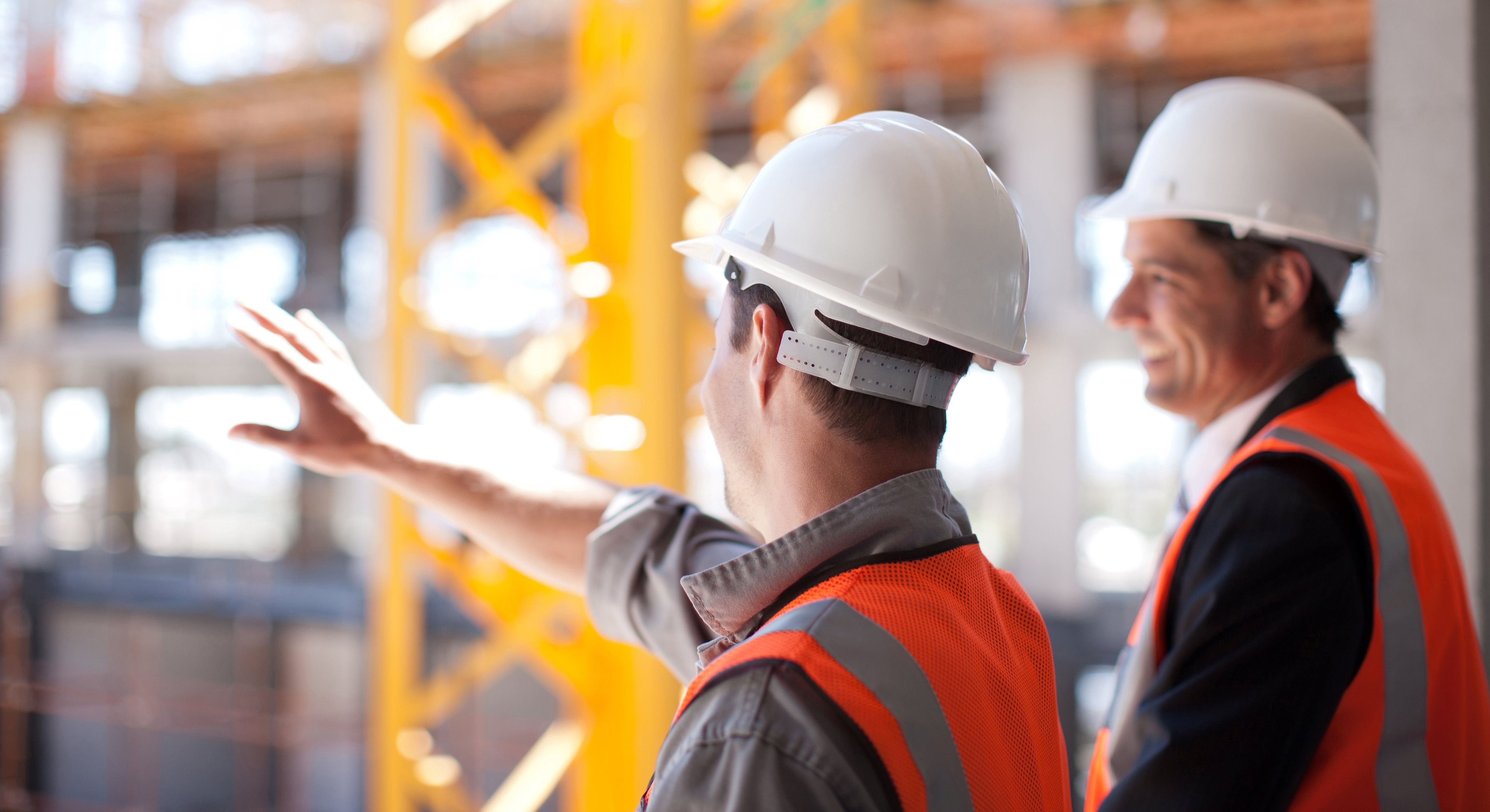two men wearing hi-vis and hard hats overlooking construction site