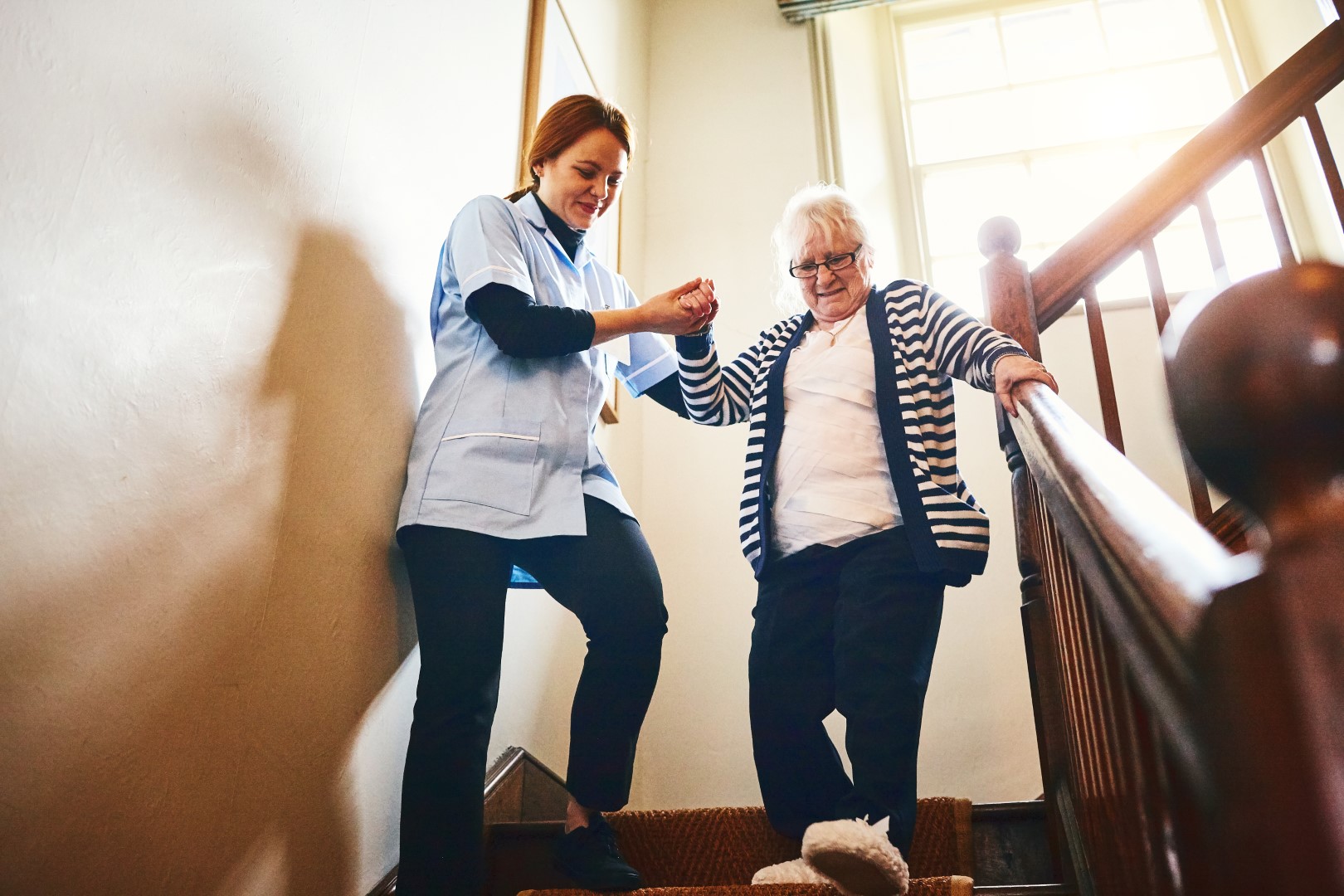 A healthcare worker helping a person walk down stairs