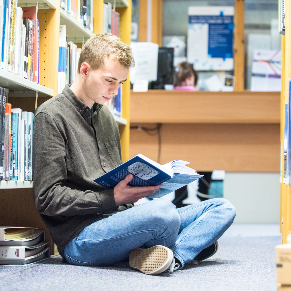 A student sitting on the floor in library reading a book