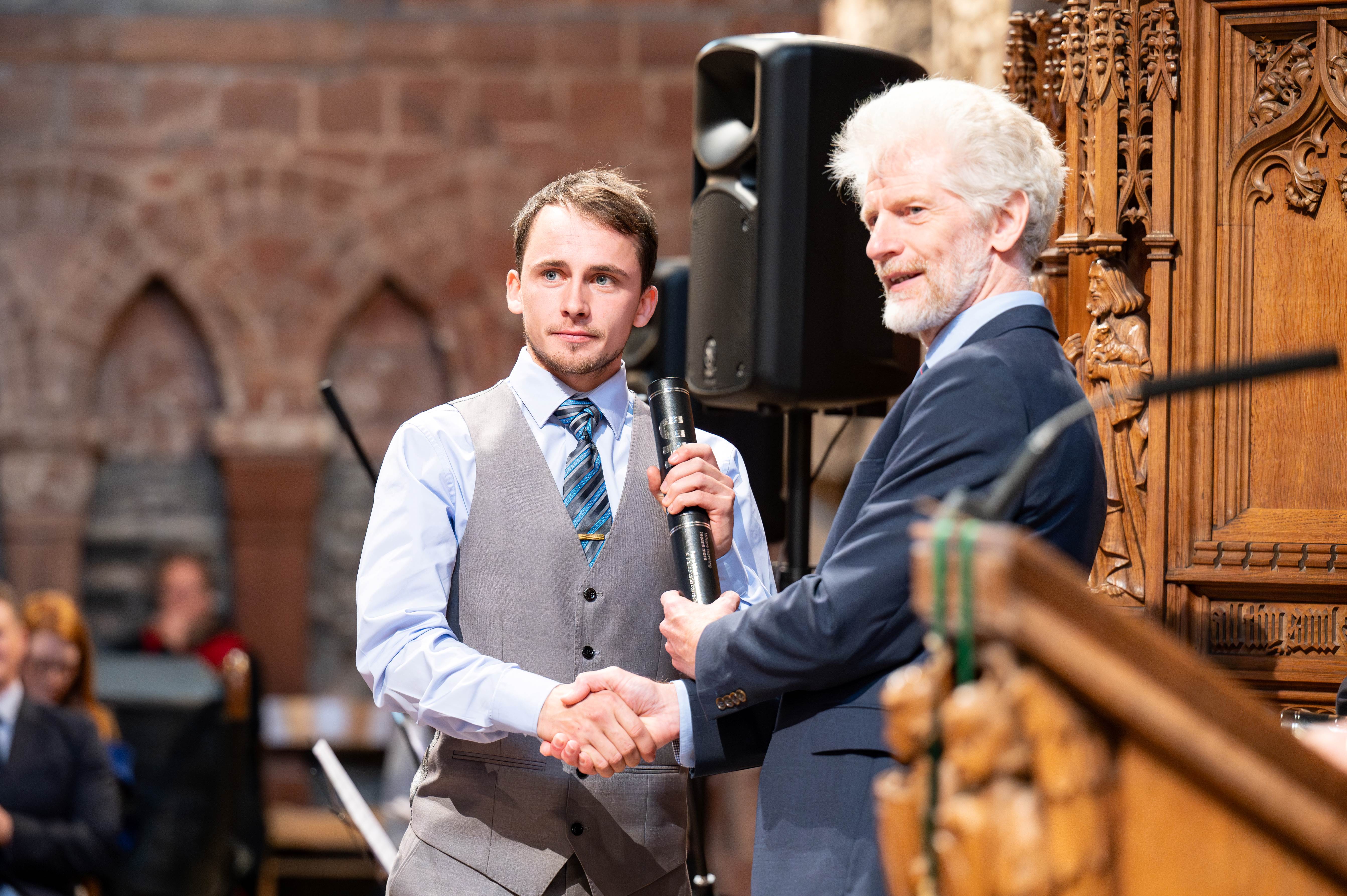 Smartly dressed male student accepting graduation scroll from presenter