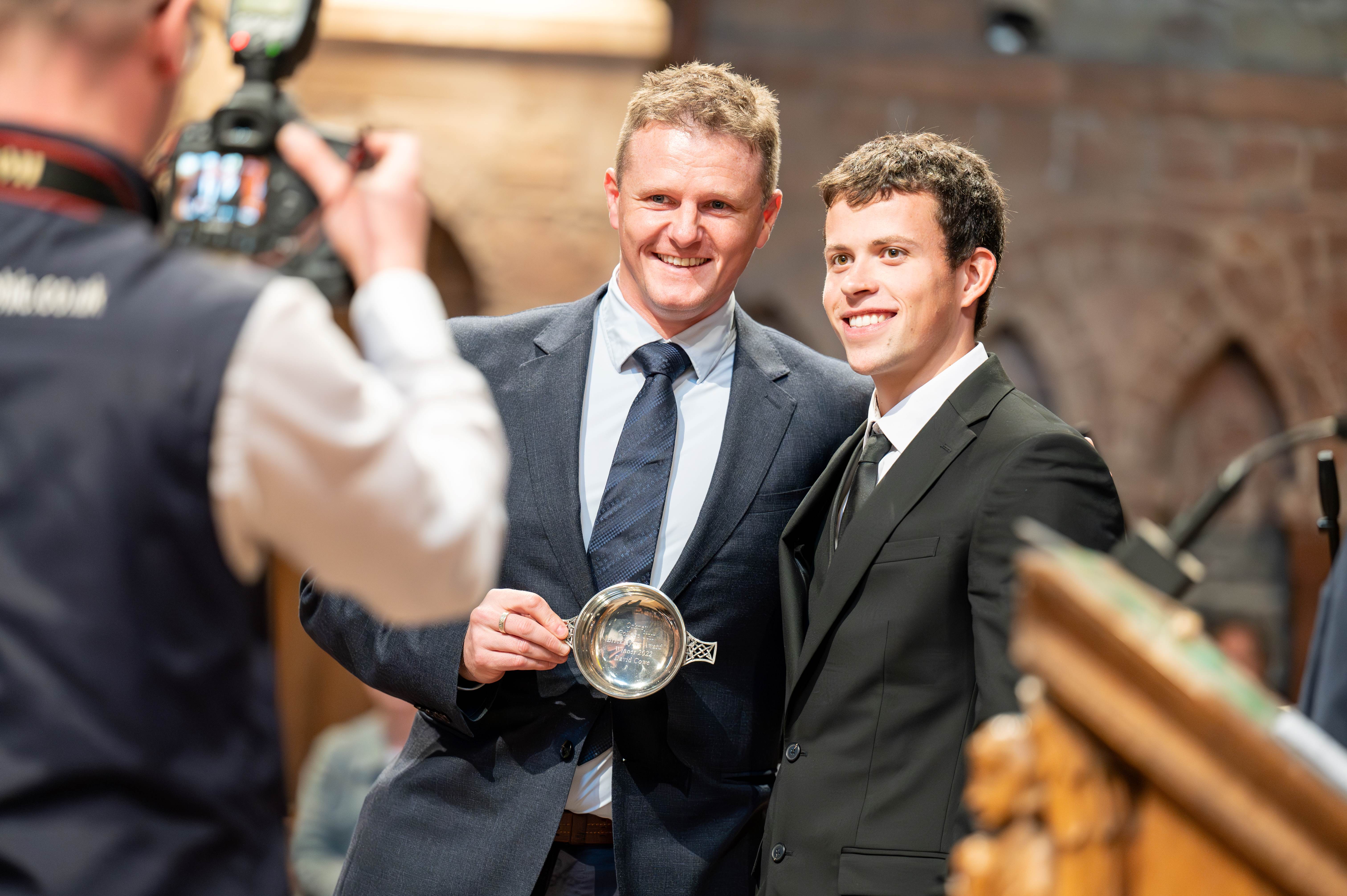 Focus on a student receiving an award, with photographer in the foreground capturing the moment Focus on a student receiving an award, with photographer in the foreground capturing the moment