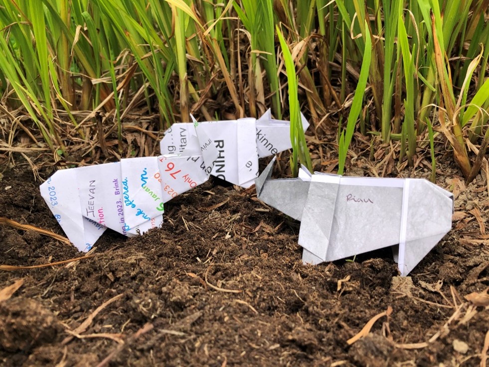 Three origami rhinos standing in grass